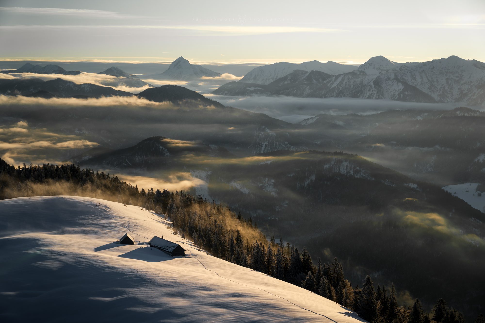 Almhütten im Schnee über einem Wolkenmeer in den Alpen