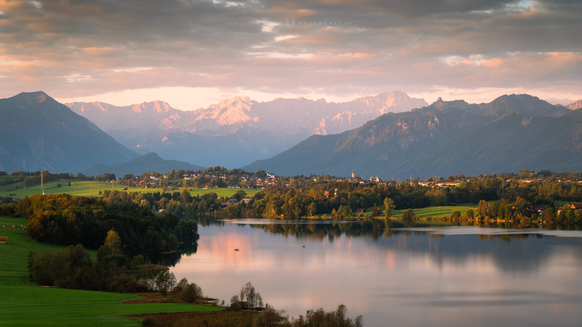 Bayerischer See mit Dorf und Alpenpanorama bei Sonnenuntergang
